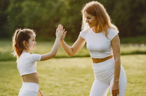 A mother and daughter high-fiving in matching outfits outdoors.