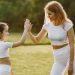 A mother and daughter high-fiving in matching outfits outdoors.